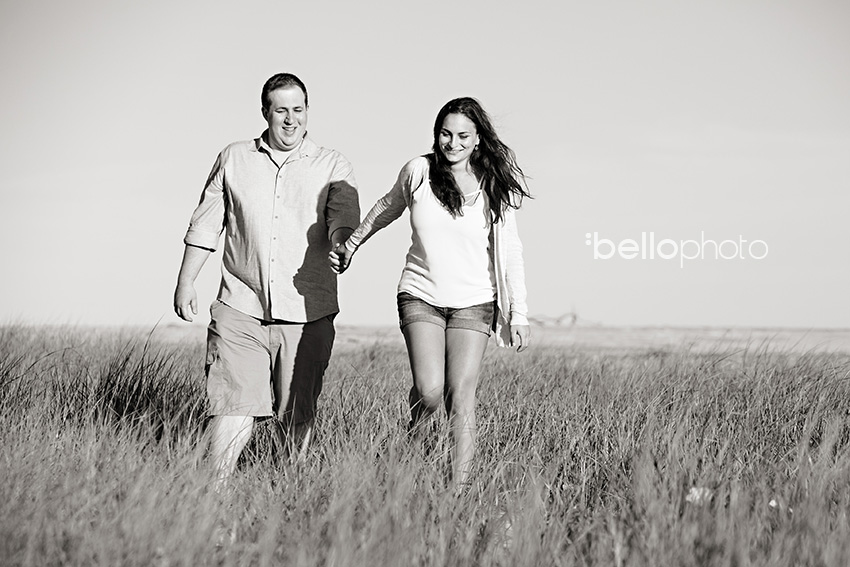 newly engaged couple walking in beach grass