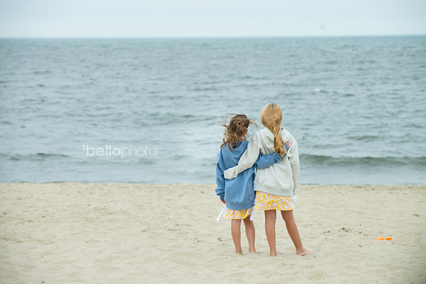 best friends, sisters, arms around each other looking at the ocean
