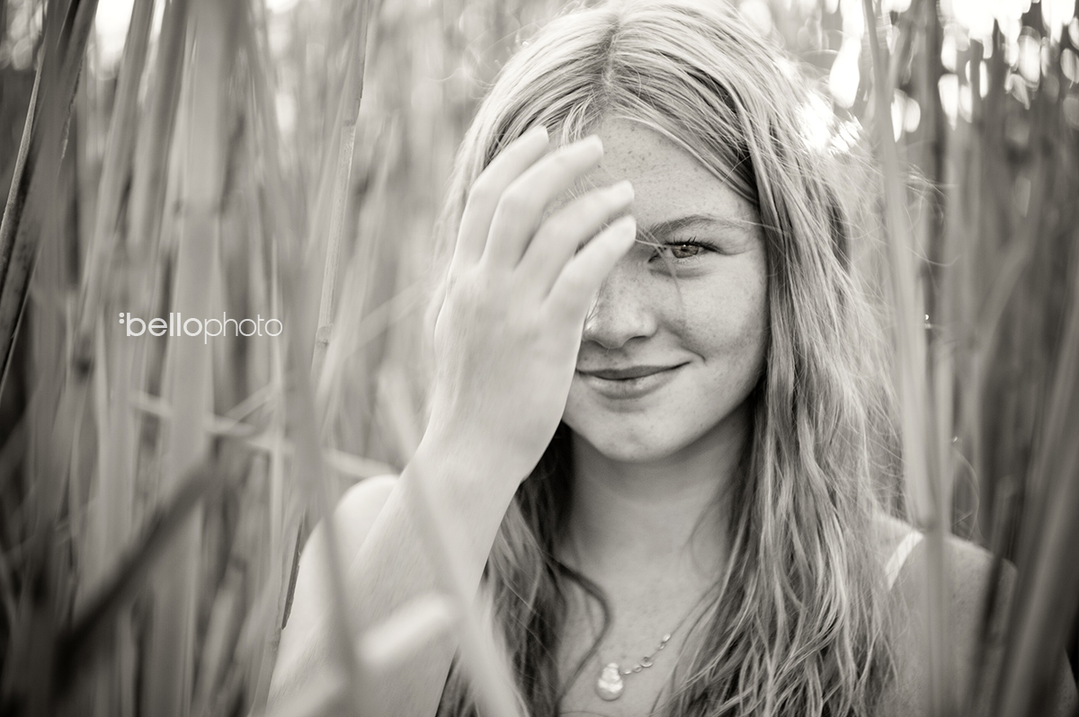 black & white photo of beautiful girl standing in beach reeds
